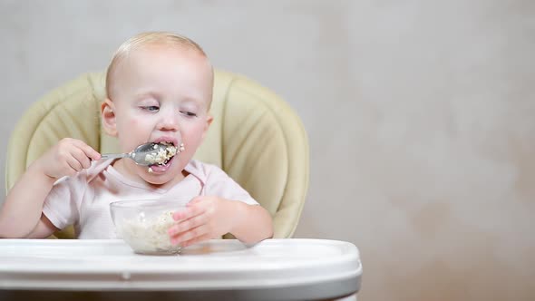 little girl learns to eat with a spoon on her own and trains on porridge. Copy space alt