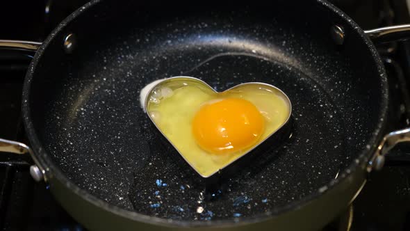 Romantic man cooking an egg with a heart for breakfast on Valentine's Day.