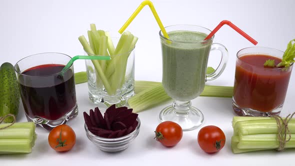 Glass mugs filled with a smoothie and juices are standing  among the ingredients for its preparation