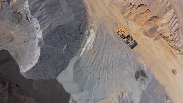 Bulldozer moving among big piles of gravels. Huge industrial territory filled with sand alt