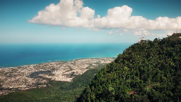 Flight over the island mountain, beach line, distant sea village and the blue ocean