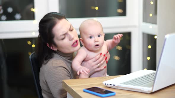 Young Woman with Toddler in Arms Typing on Laptop Remote Work with a Baby at Home