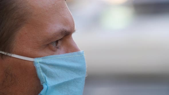 Profile of a Young Man Wearing a Disposable Medical Mask on a City Street. Man in Mask Looking at