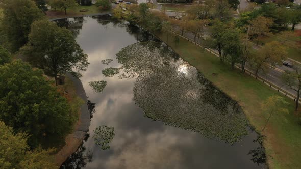 A drone shot of a pond on a cloudy day. The camera dolly in over the pond as the sun shines through alt