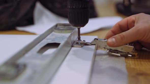 Carpenter Man Screws Hinge to Furniture Door Using Electric Screwdriver Hands Closeup Side View alt