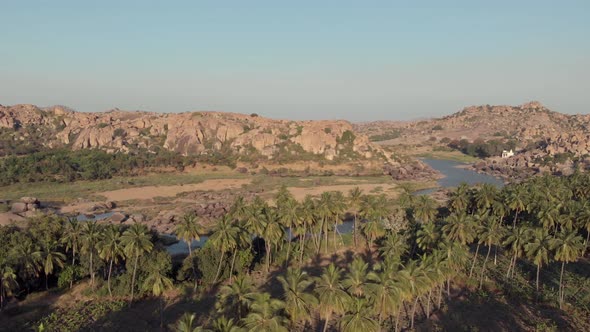 Paradisiac Tungabhadra Riverbank among rocky landscape and lush palm trees in Hampi, India alt