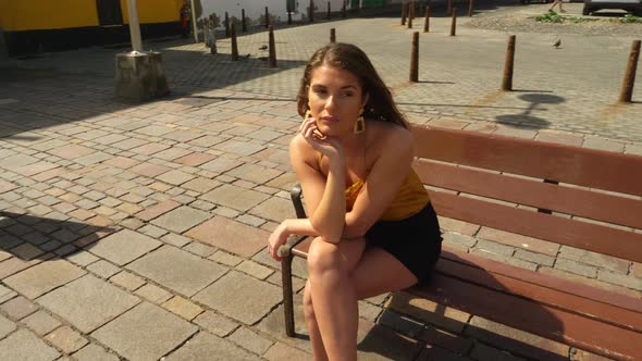 Beautiful Female Sitting by the Park Bench With Her Legs Crossed alt