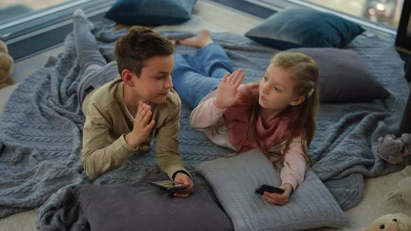 Cute Siblings Using Smartphones Indoors. Children Giving High Five. alt