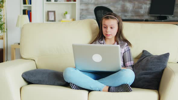 Sweet Little Girl with Braces Sitting on the Couch Using Her Laptop alt