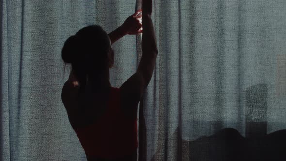 Young Woman in Sports Clothes Opens the Curtains and Lets Light Into the Room alt