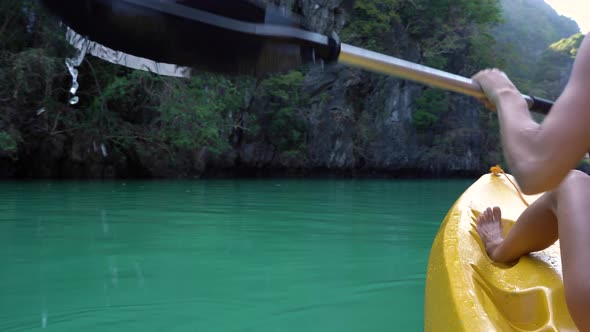 Woman paddles yellow kayak in the lake with turquoise water.  alt