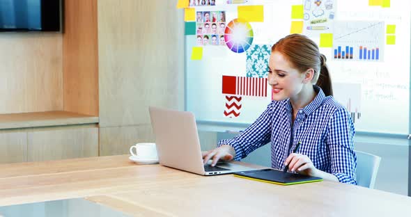 Female graphic designer using laptop and graphic tablet in conference room alt
