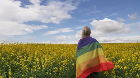 Female with LGBT rainbow flag on yellow rapeseed field in spring alt