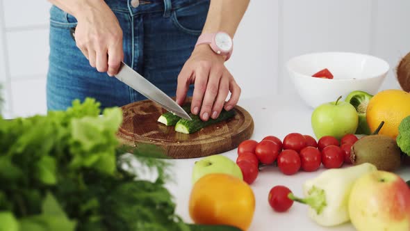 Female cook cuts a fresh green cucumber with a knife on a wooden cutting board alt