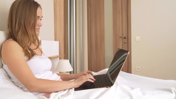 Woman Typing on Laptop in Bed. alt