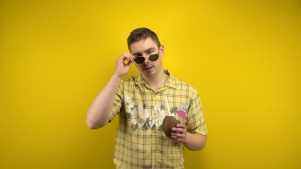 A Man in Sunglasses and a Hawaiian Shirt Takes Off His Glasses and Holds a Coconut Pina Colada in alt