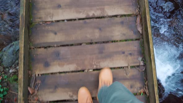Close-up of legs of male traveler walking across a bridge to mountain river. alt