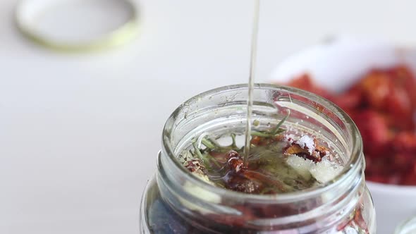 A Woman Pours Olive Oil Over Sun Dried Tomatoes In A Jar. Cooking At Home. Close Up Shot alt