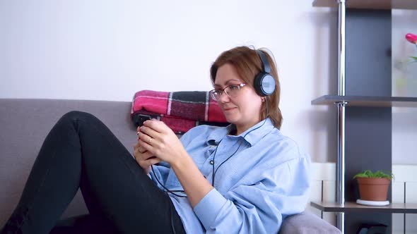 Woman lying on the couch, uses a smartphone in headphones.