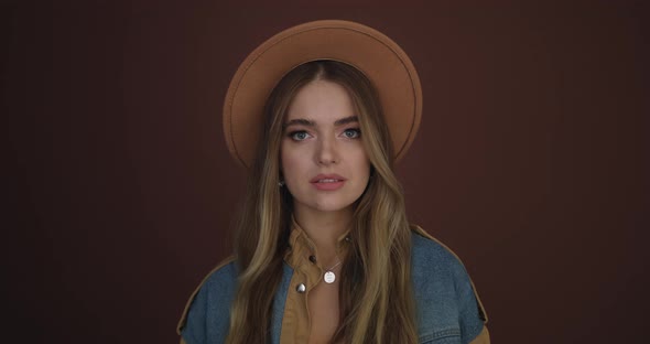 Attractive Young Woman Posing with a Brown Hat Smiling at the Camera on a Brown Background alt