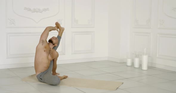 Flexible and Plastic Male Yogi with a Beard Doing Yoga on a Rug in a Bright Studio. He Does alt