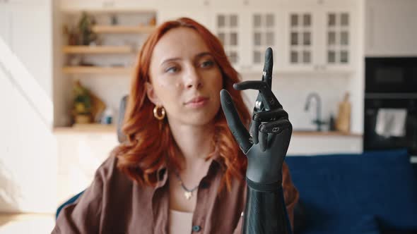 Young Redhaired Woman Looks at Her Bionic Prosthetic Left Hand and Alternately Flexes and Unbends alt