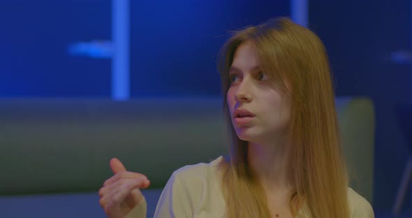 Portrait Beautiful Woman Blogger Speaks and Gesticulates Interview in a Room with Blue Lighting alt