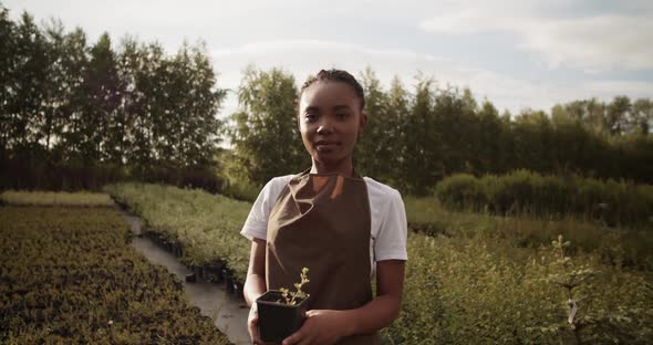 Young Black Farmer with Potted Plant in Countryside alt