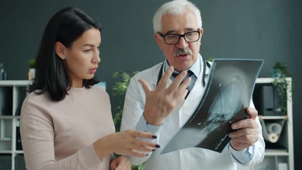 Patient and Doctor Looking at X-ray Image Talking Indoors in Office in Hospital alt