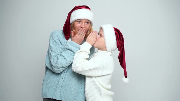 Happy Young Girl and Boy in Santa Claus Caps Whispering and Laughing