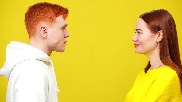 Young Millennial Redhead Couple Looking at Each Other at Yellow Background Smiling alt