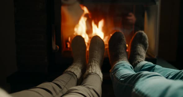 Legs and Feet in Woolen Socks Warming Up By Fireplace Flame in Cozy Room