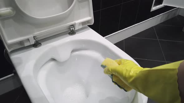 Cleaning lady in yellow gloves washes the toilet bowl in the toilet. First-person view. pov