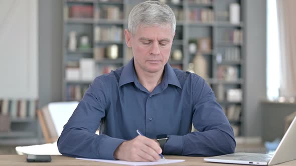 Serious Middle Aged Man Writing on Papers While Working in Office alt