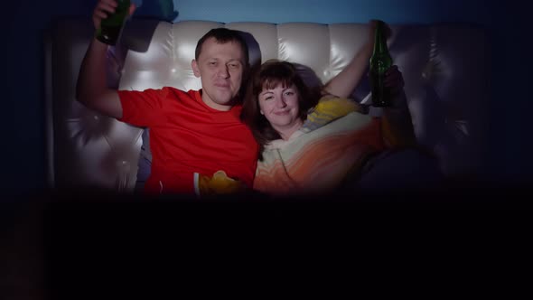 Happy Man and Woman Lie on the Bed Watching Tv Drink Beer and Dance in the Evening