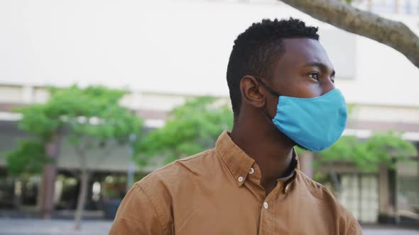 African american businessman wearing face mask sitting in park alt
