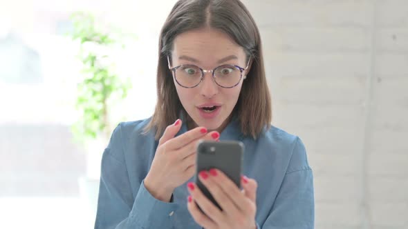 Young Woman Reacting to Loss on Smartphone in Office alt