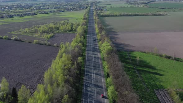 Aerial view of cars driving along the empty roadriding along trees and fields on sunny morning alt