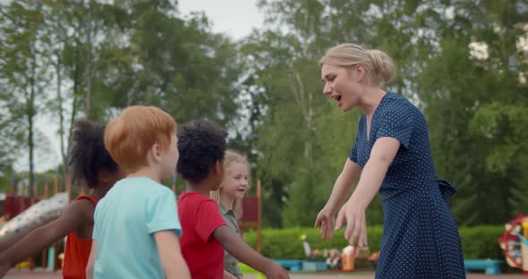 Group of Diverse Kindergarten Students Hugging Teacher at Playground alt