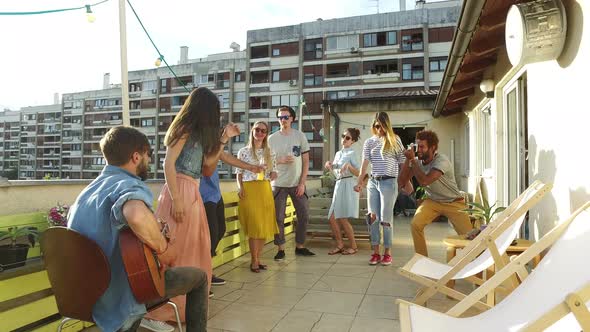 Happy people dancing and playing guitar at the rooftop party on sunny day alt