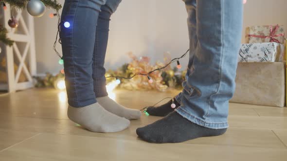 Legs of Unrecognizable Man and Woman Standing at Home with Christmas Garland Shining alt