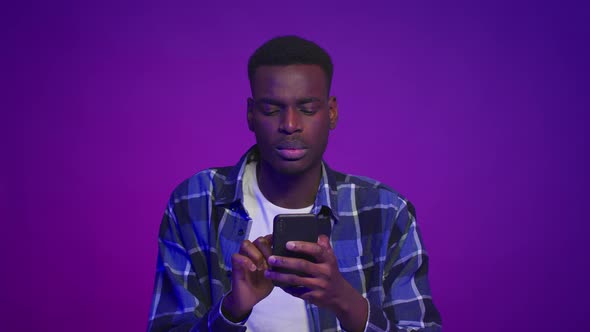 Serious Black Guy Texting Using Mobile Phone Over Purple Background alt