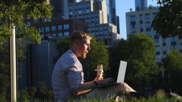 a man works at a laptop and eats fast food while sitting in a park overlooking the city