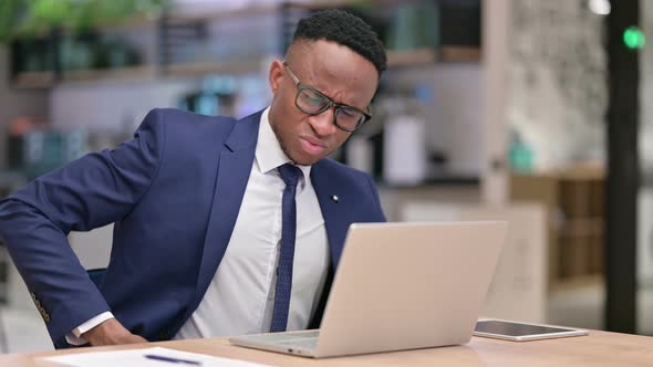 Tired African Businessman with Laptop Having Back Pain in Office  alt