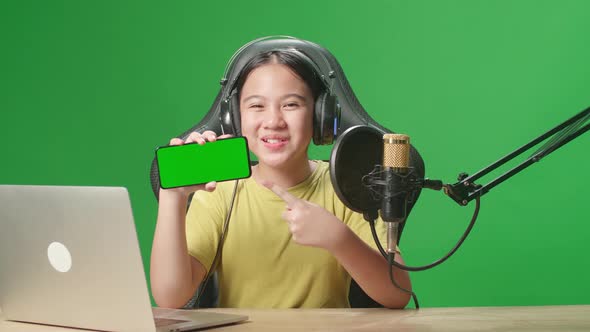 Asian Kid Girl Holding Phone With Mock Up Green Screen While Live Stream In Green Screen Studio alt