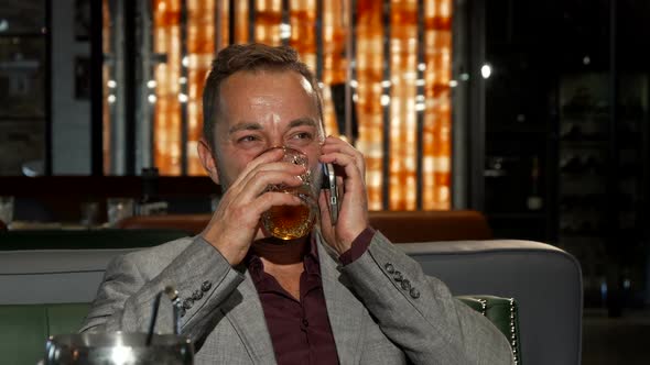 Cheerful Businessman Drinking Whiskey While Talking on the Phone alt