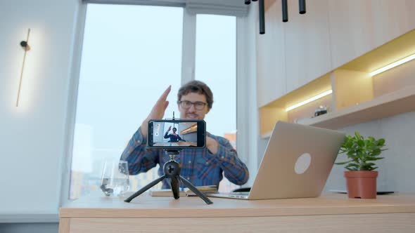 Young blogger writes a video for a blog using a smartphone while sitting at a laptop at home. alt