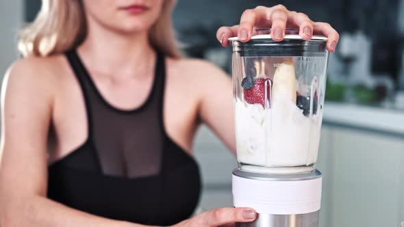 A young blonde woman making a milkshake of fruits and berries alt