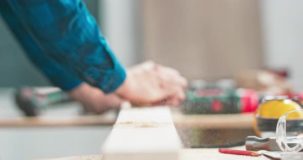 A Bearded Handyman is Sanding Wood for Furniture in a Carpentry Workshop alt