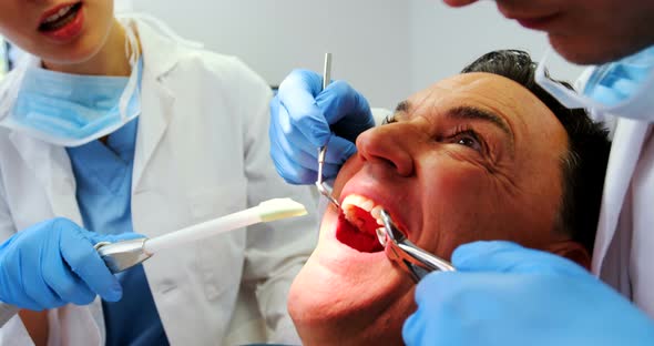 Dentists examining a male patient with tools alt